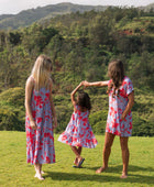 little girl with brown hair wearing a mid length dress with periwinkle background and bright red hibiscus print.