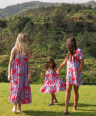 little girl with brown hair wearing a mid length dress with periwinkle background and bright red hibiscus print.