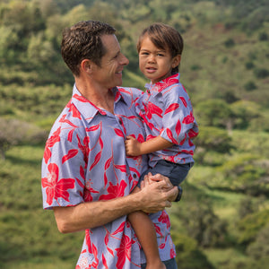 man with brown hair wearing a button up aloha shirt with periwinkle background and bright red hibiscus print.