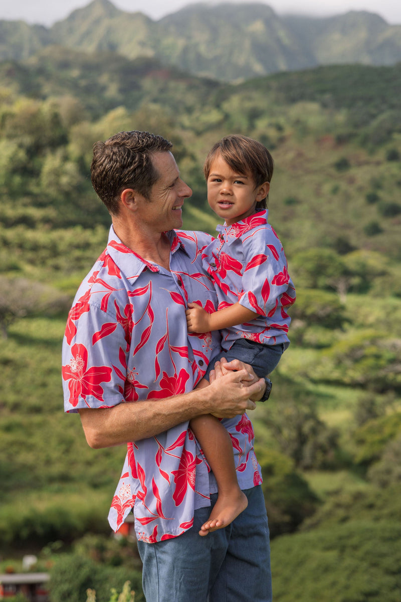 man with brown hair wearing a button up aloha shirt with periwinkle background and bright red hibiscus print.