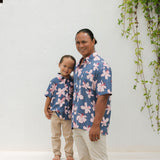 man wearing button up aloha shirt in navy and pink hibiscus print.