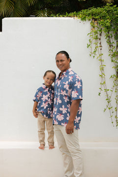 man wearing button up aloha shirt in navy and pink hibiscus print.