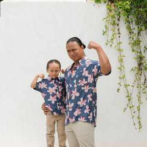 little boy wearing button up aloha shirt in navy and pink hibiscus print.