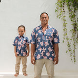 man wearing button up aloha shirt in navy and pink hibiscus print.