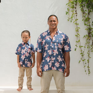 man wearing button up aloha shirt in navy and pink hibiscus print.