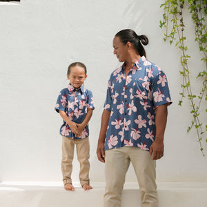 man wearing button up aloha shirt in navy and pink hibiscus print.