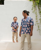 man wearing button up aloha shirt in navy and pink hibiscus print.