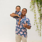 man wearing button up aloha shirt in navy and pink hibiscus print.