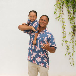 man wearing button up aloha shirt in navy and pink hibiscus print.