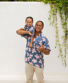 man wearing button up aloha shirt in navy and pink hibiscus print.
