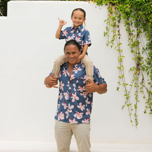 little boy wearing button up aloha shirt in navy and pink hibiscus print.