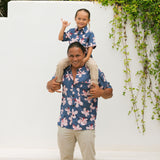 man wearing button up aloha shirt in navy and pink hibiscus print.