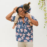 man wearing button up aloha shirt in navy and pink hibiscus print.
