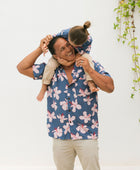 man wearing button up aloha shirt in navy and pink hibiscus print.