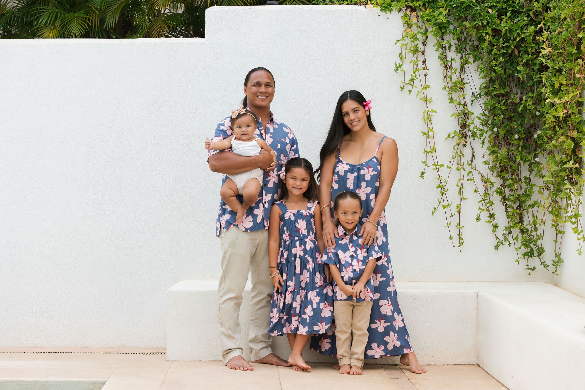 little boy wearing button up aloha shirt in navy and pink hibiscus print.