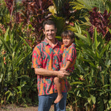 man with brown hair wearing a colorful button up aloha shirt with tropical lei print
