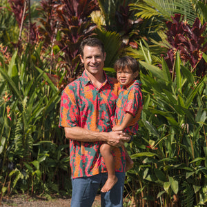 man with brown hair wearing a colorful button up aloha shirt with tropical lei print