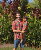 man with brown hair wearing a colorful button up aloha shirt with tropical lei print