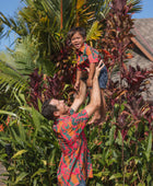 boy with brown hair wearing a colorful button up aloha shirt with tropical lei print