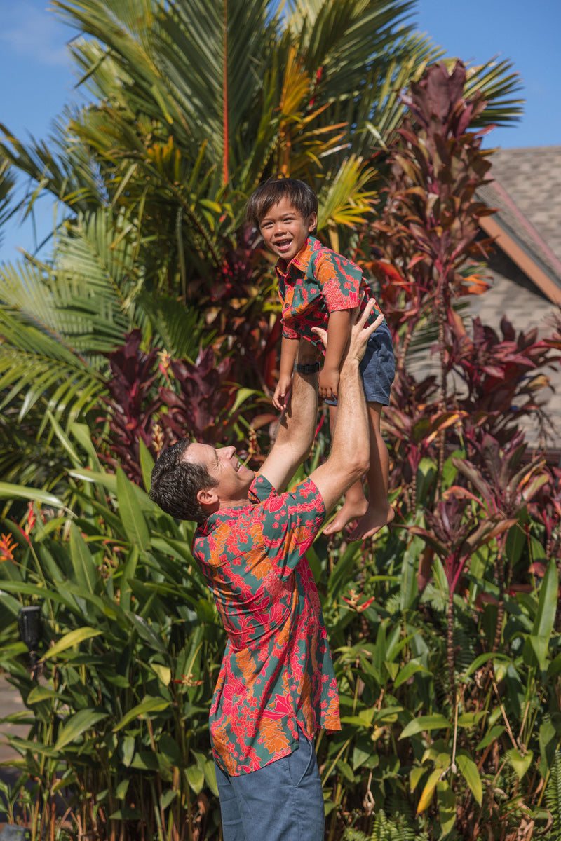 boy with brown hair wearing a colorful button up aloha shirt with tropical lei print