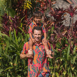 man with brown hair wearing a colorful button up aloha shirt with tropical lei print