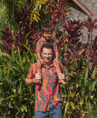 man with brown hair wearing a colorful button up aloha shirt with tropical lei print