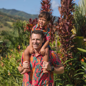 man with brown hair wearing a colorful button up aloha shirt with tropical lei print