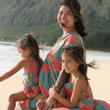 little girl wearing a green knee length dress with orange and yellow lei pua print 
