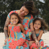 little girl wearing a green knee length dress with orange and yellow lei pua print 