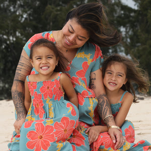 little girl wearing a green knee length dress with orange and yellow lei pua print 