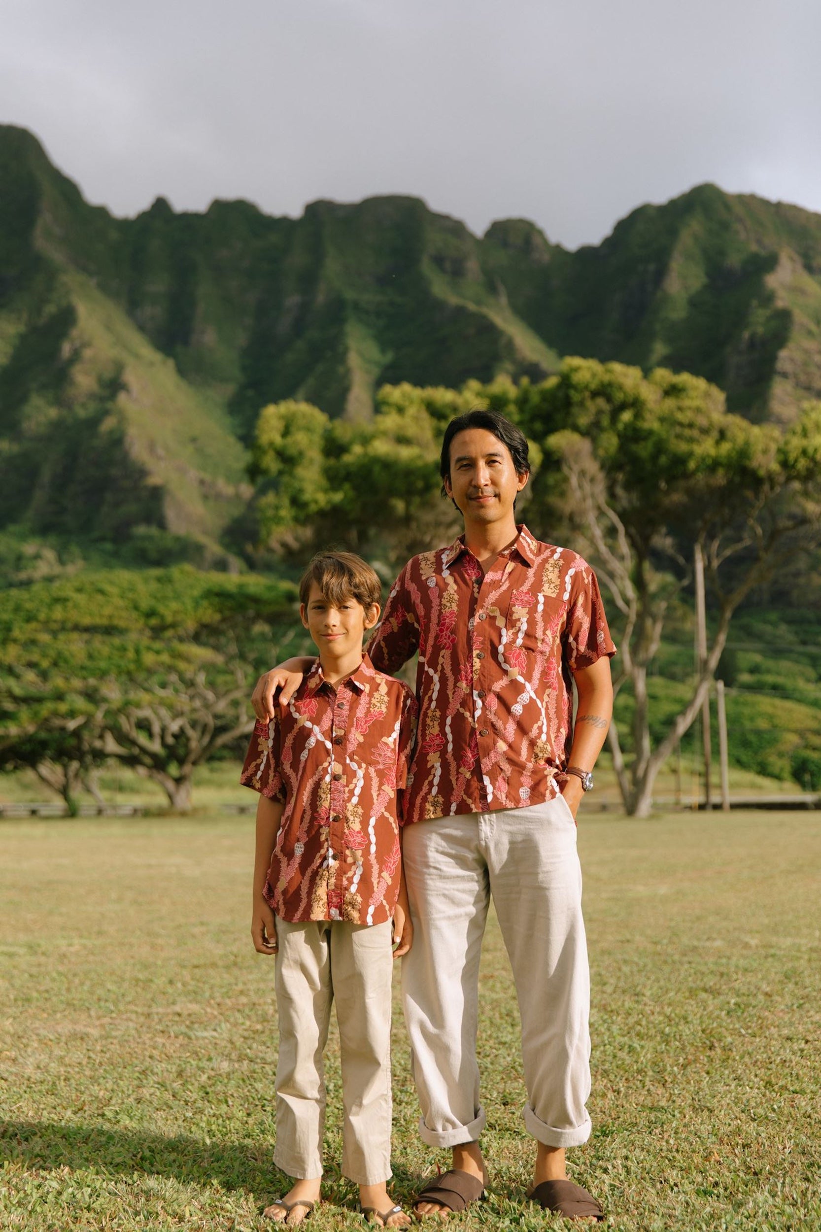 man with black hair wearing a red-brown aloha button up shirt with lei print