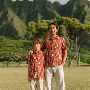 man with black hair wearing a red-brown aloha button up shirt with lei print