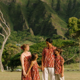 little girl wearing a red-brown tie back dress with ruffle hem and lei print