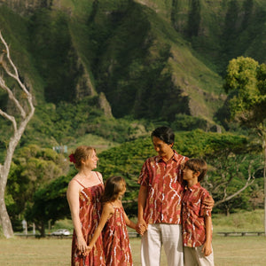 little girl wearing a red-brown tie back dress with ruffle hem and lei print