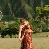little girl wearing a red-brown tie back dress with ruffle hem and lei print