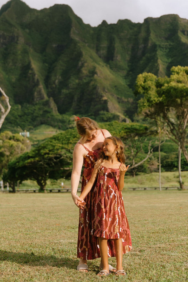 little girl wearing a red-brown tie back dress with ruffle hem and lei print