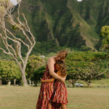 little girl wearing a red-brown tie back dress with ruffle hem and lei print