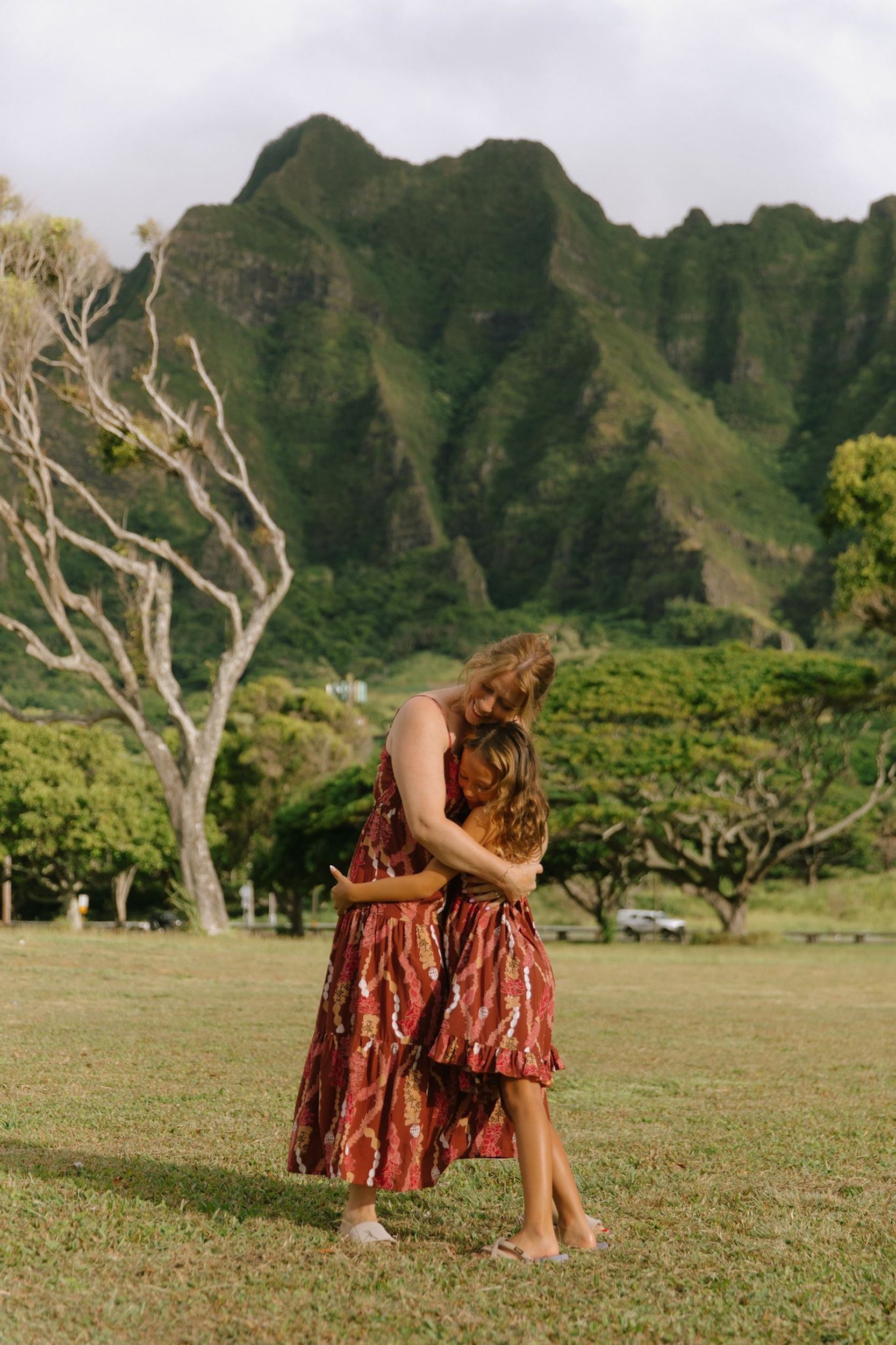 little girl wearing a red-brown tie back dress with ruffle hem and lei print