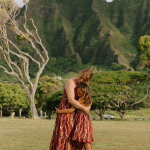 little girl wearing a red-brown tie back dress with ruffle hem and lei print