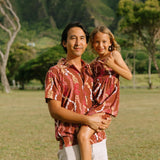 man with black hair wearing a red-brown aloha button up shirt with lei print