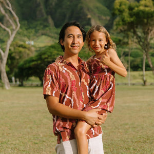 man with black hair wearing a red-brown aloha button up shirt with lei print