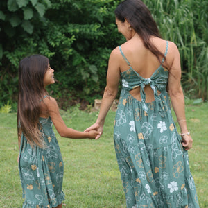 little girl wearing lush green tie back dress with puakenikeni print