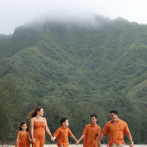 man with brown hair wearing an orange aloha button up shirt with puakenikeni print