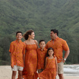 little girl wearing an orange flowy dress with puakenikeni print
