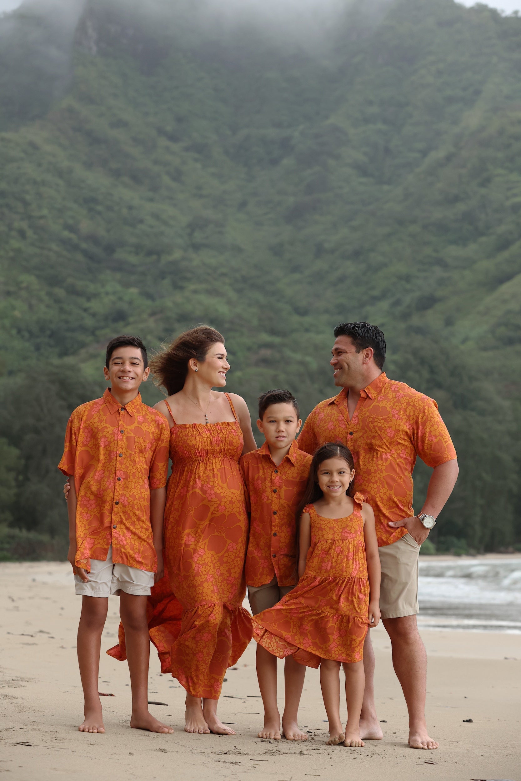 little girl wearing an orange flowy dress with puakenikeni print