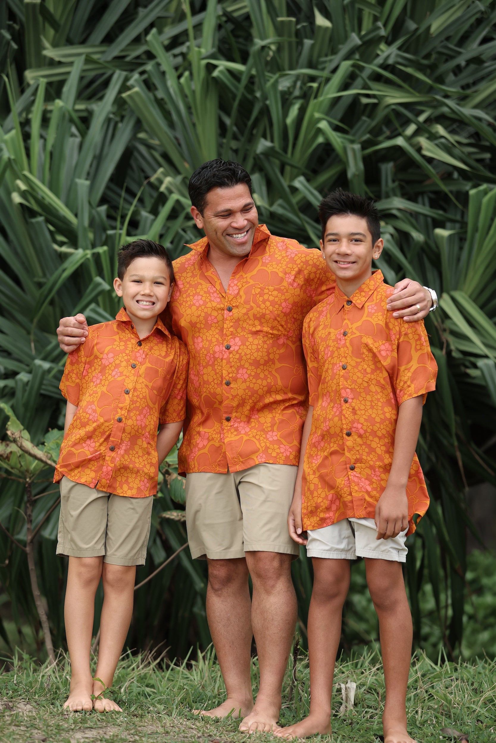 man with brown hair wearing an orange aloha button up shirt with puakenikeni print