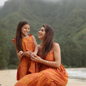 little girl wearing an orange flowy dress with puakenikeni print