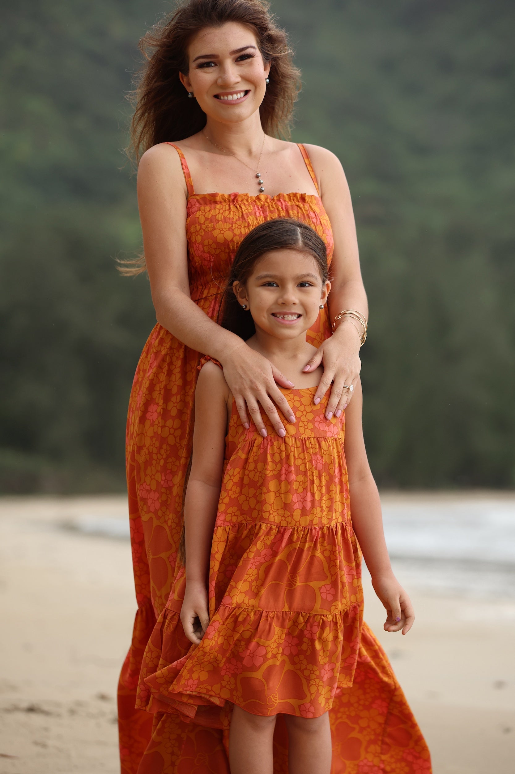 little girl wearing an orange flowy dress with puakenikeni print