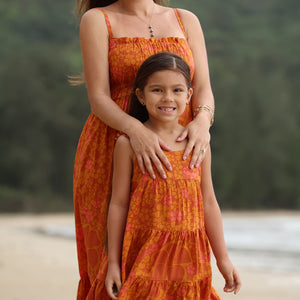 little girl wearing an orange flowy dress with puakenikeni print