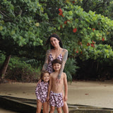 little boy wearing board shorts  in blush and brown hibiscus print.